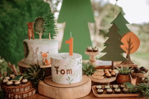 Woodland themed first birthday party dessert table with fox decorations and number one candle.