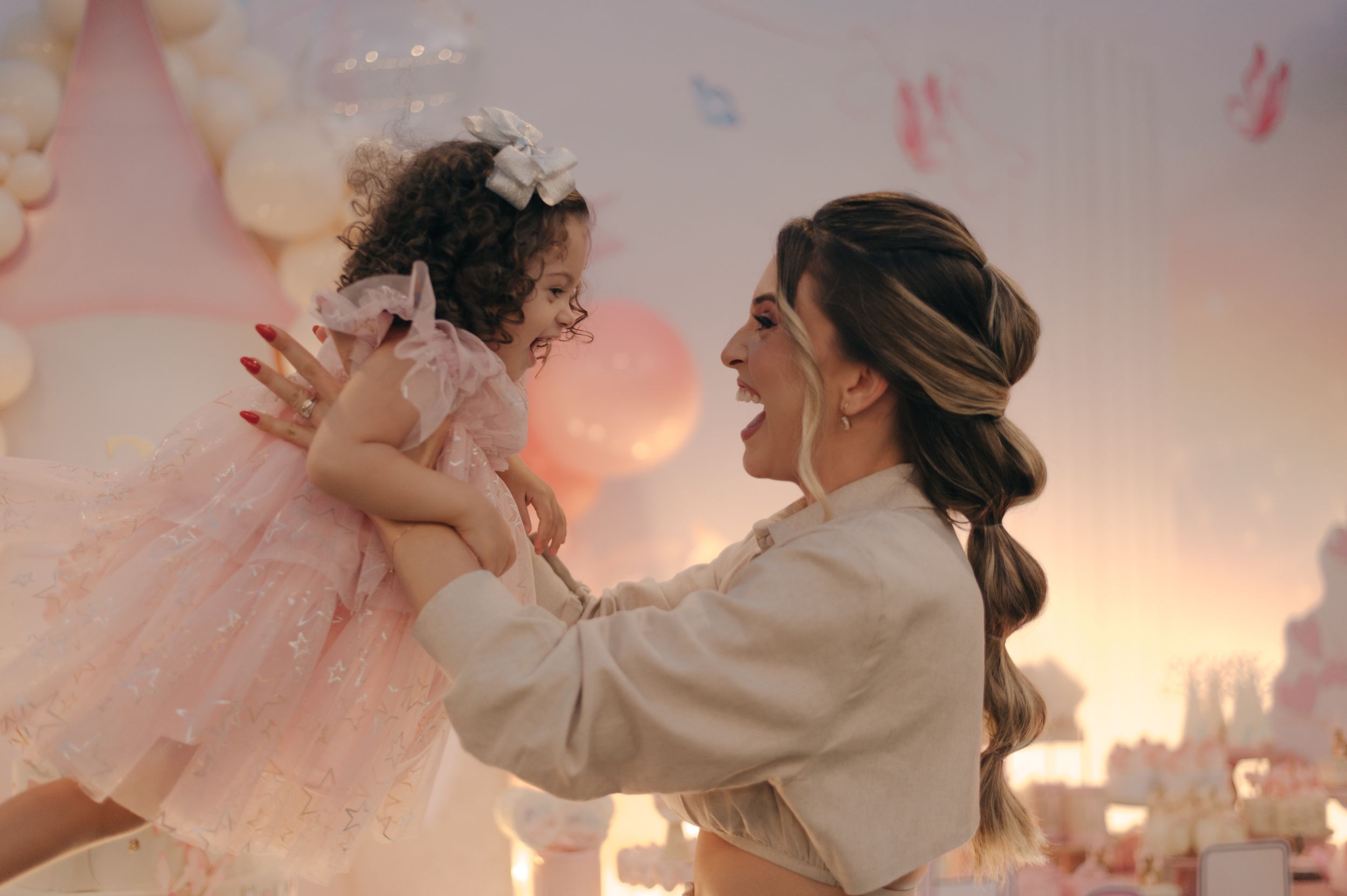 Joyful celebration moment with mother lifting child in pink dress.