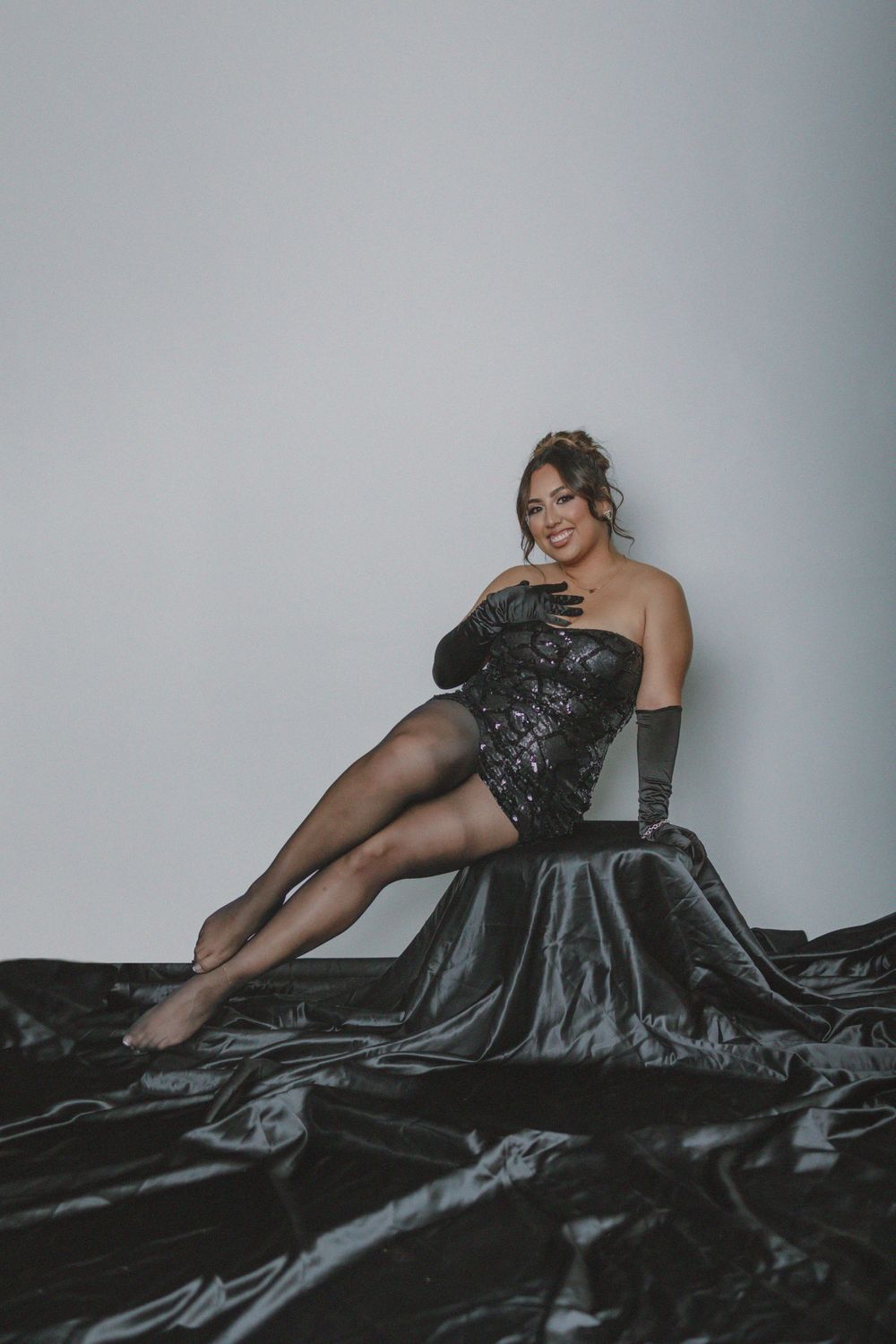 Glamour shot of model reclining on black satin fabric wearing sequined dress and long gloves.