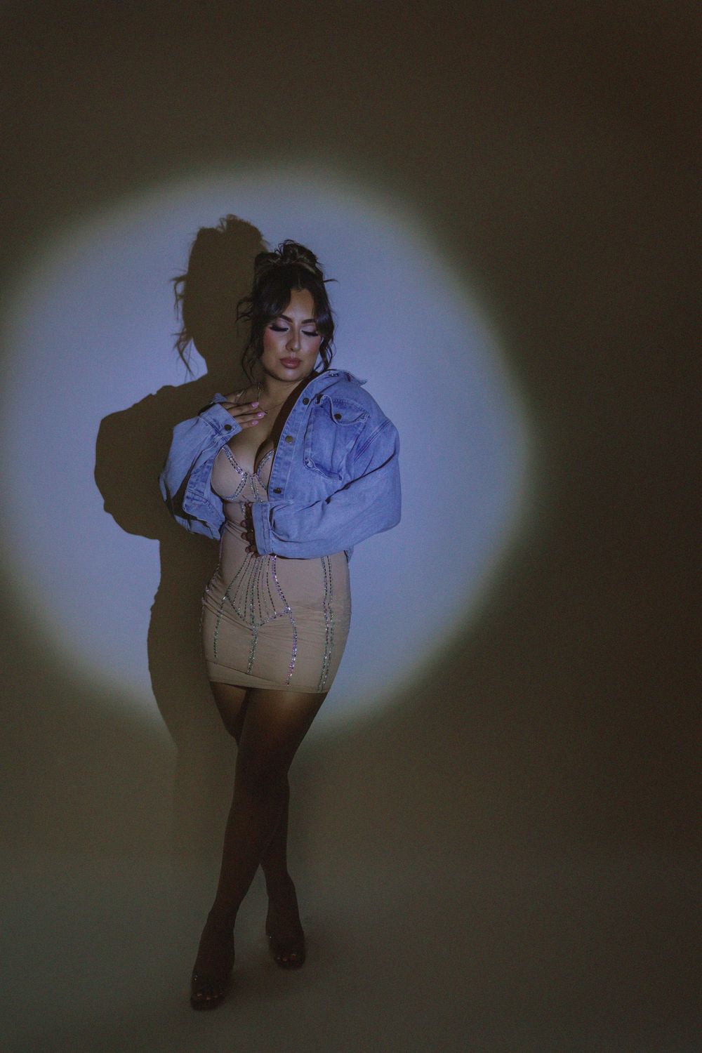 Model poses in denim jacket and shorts against blue spotlight backdrop showing confident stance.