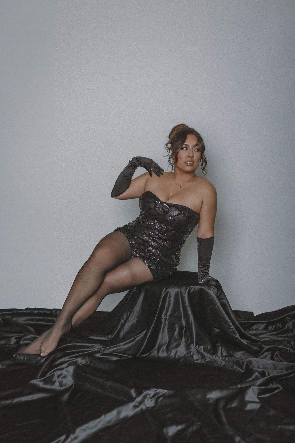 Woman in black evening gown posing on dark fabric.