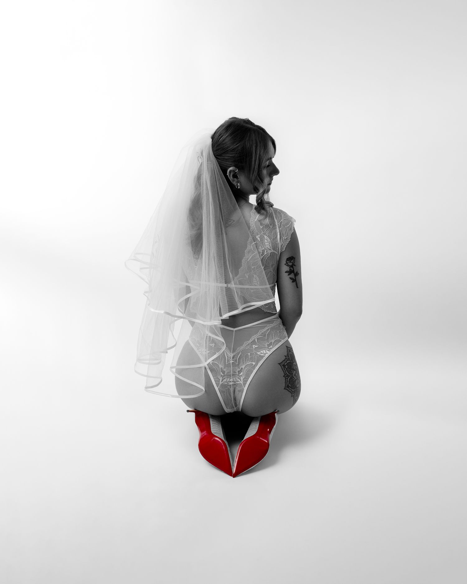 Artistic black and white photo of person in white lingerie and red shoes with bridal veil.