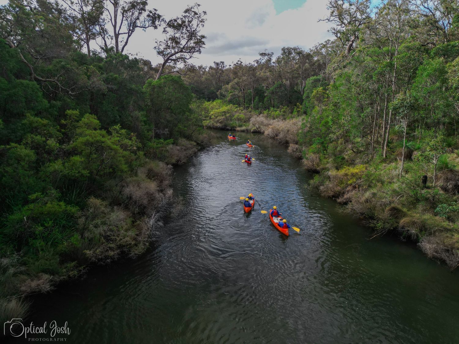 Drone shot of two red kayaks paddling down a scenic forest river. (Optical Josh)