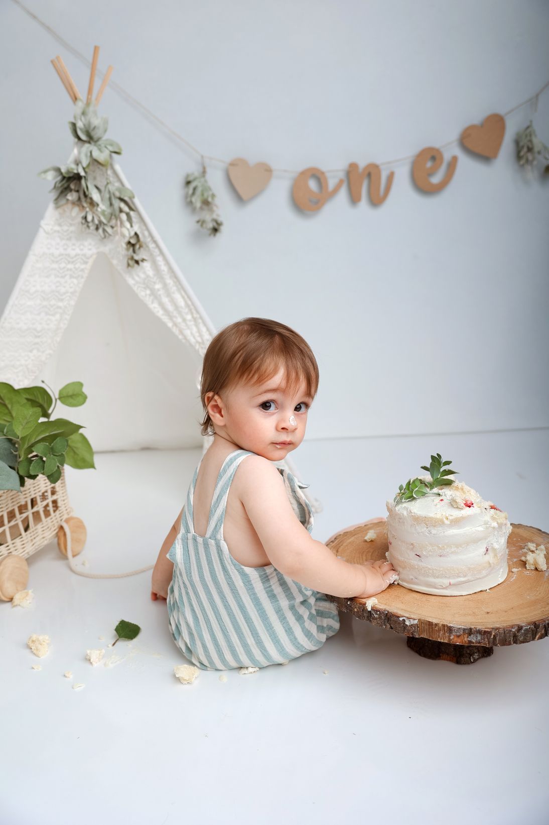 First birthday setup with teepee, cake on wooden stand, and kraft paper banner decoration.