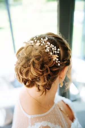 Elegant bridal updo with curls adorned with a gold floral hair comb with pearl accents, viewed from behind.