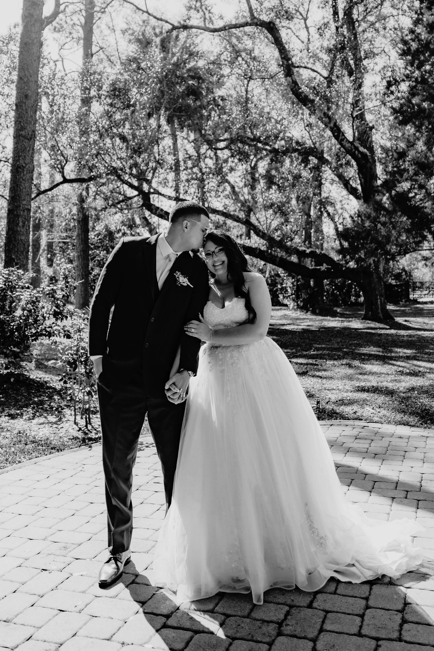 A wedding couple runs playfully through a sunlit forest path with flowing white dress and navy suit.