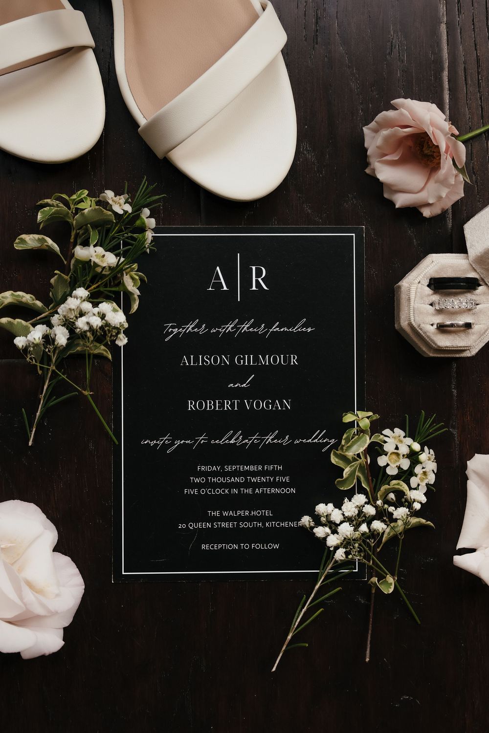 Elegant black and white wedding invitation suite with delicate pink roses and white flowers on dark background.