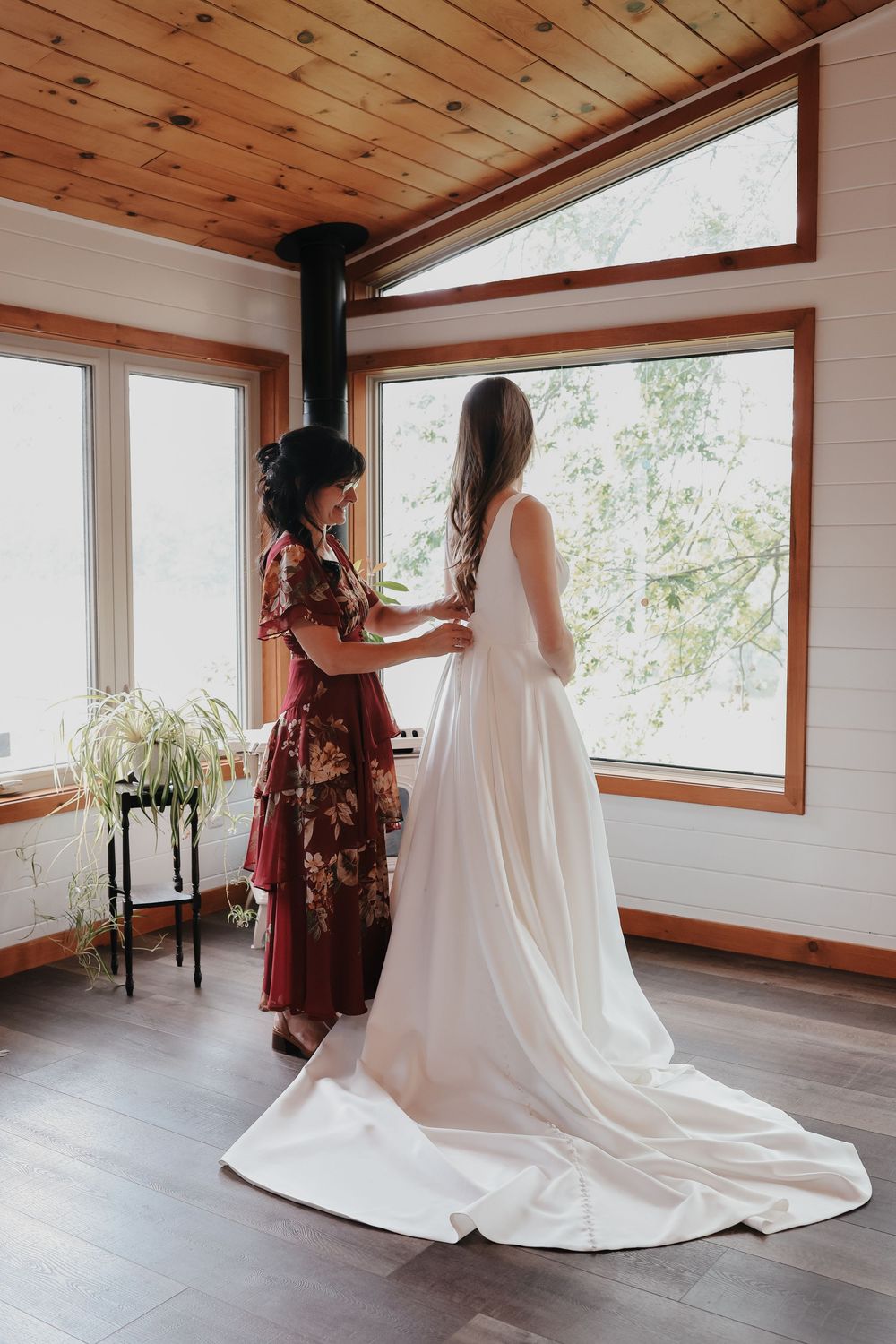 Bridal preparation scene with flowing white wedding dress in a rustic wood-paneled room with large windows.