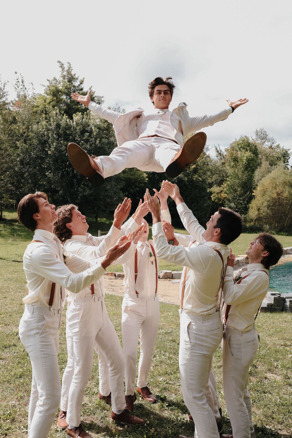 A group wearing all white outfits performs a coordinated trust fall sequence outdoors in a grassy area.