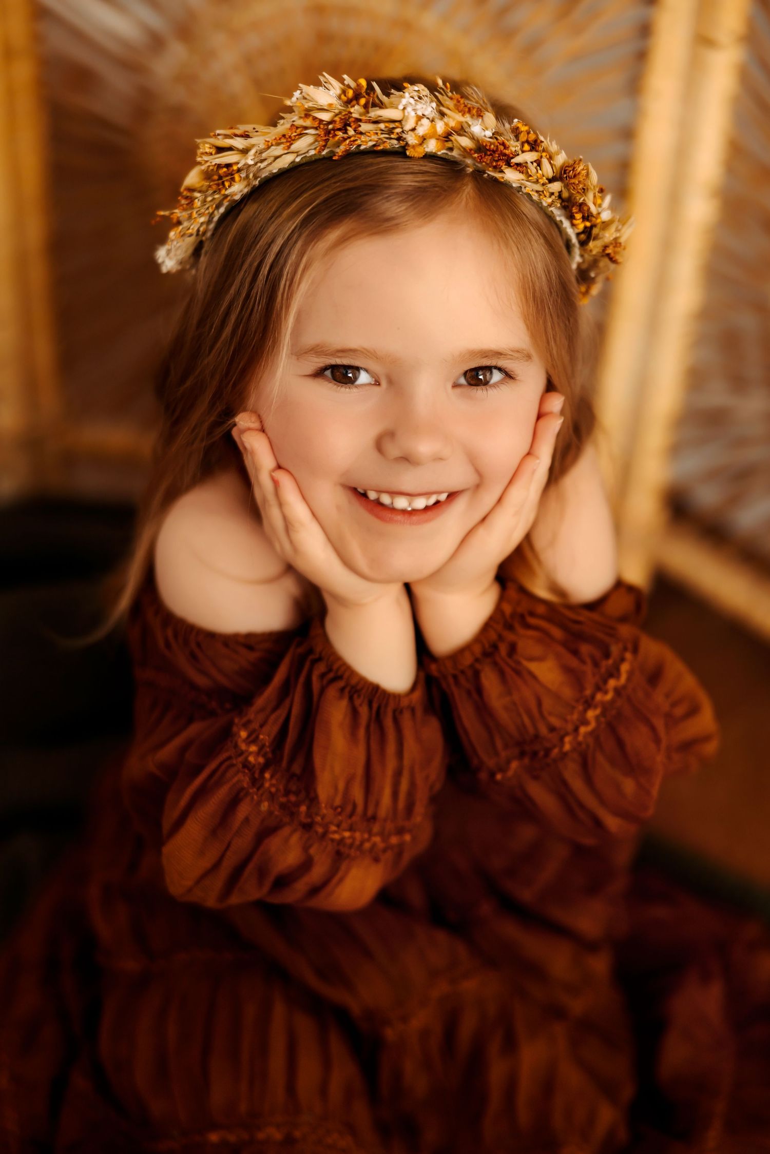 A whimsical portrait of someone wearing a brown dress and golden leaf crown in warm, glowing lighting.