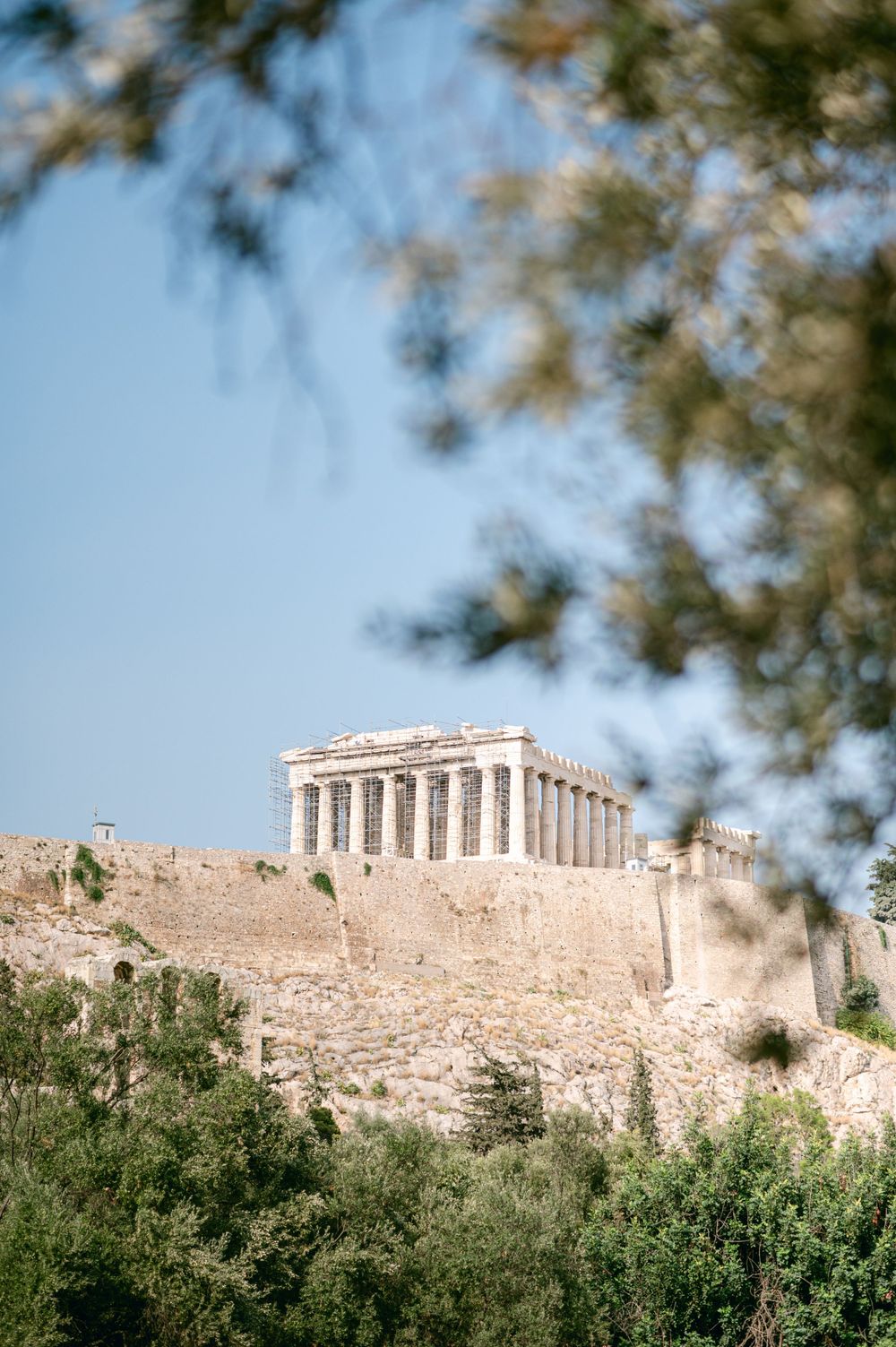 The Parthenon temple sits atop the Acropolis hill against a blue sky in Athens.
