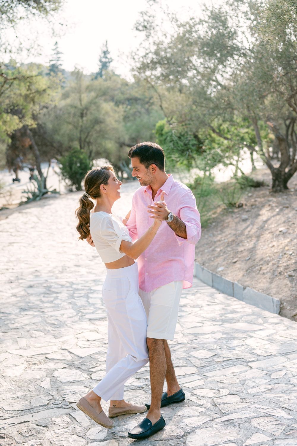 A couple in matching white and pink outfits dance together on a stone pathway.