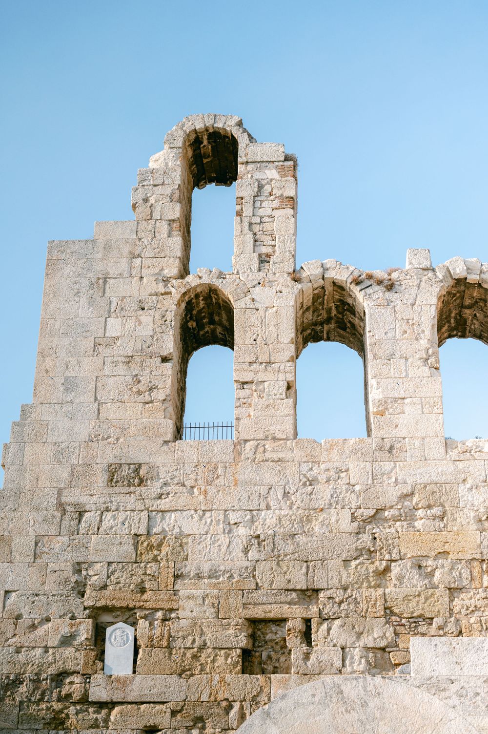 Ancient stone arches with multiple openings stand against a bright blue sky.