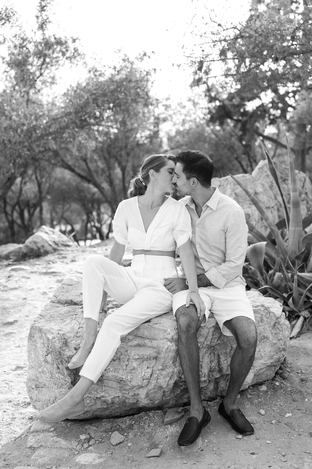 A couple sits together on a large rock during an outdoor photoshoot.