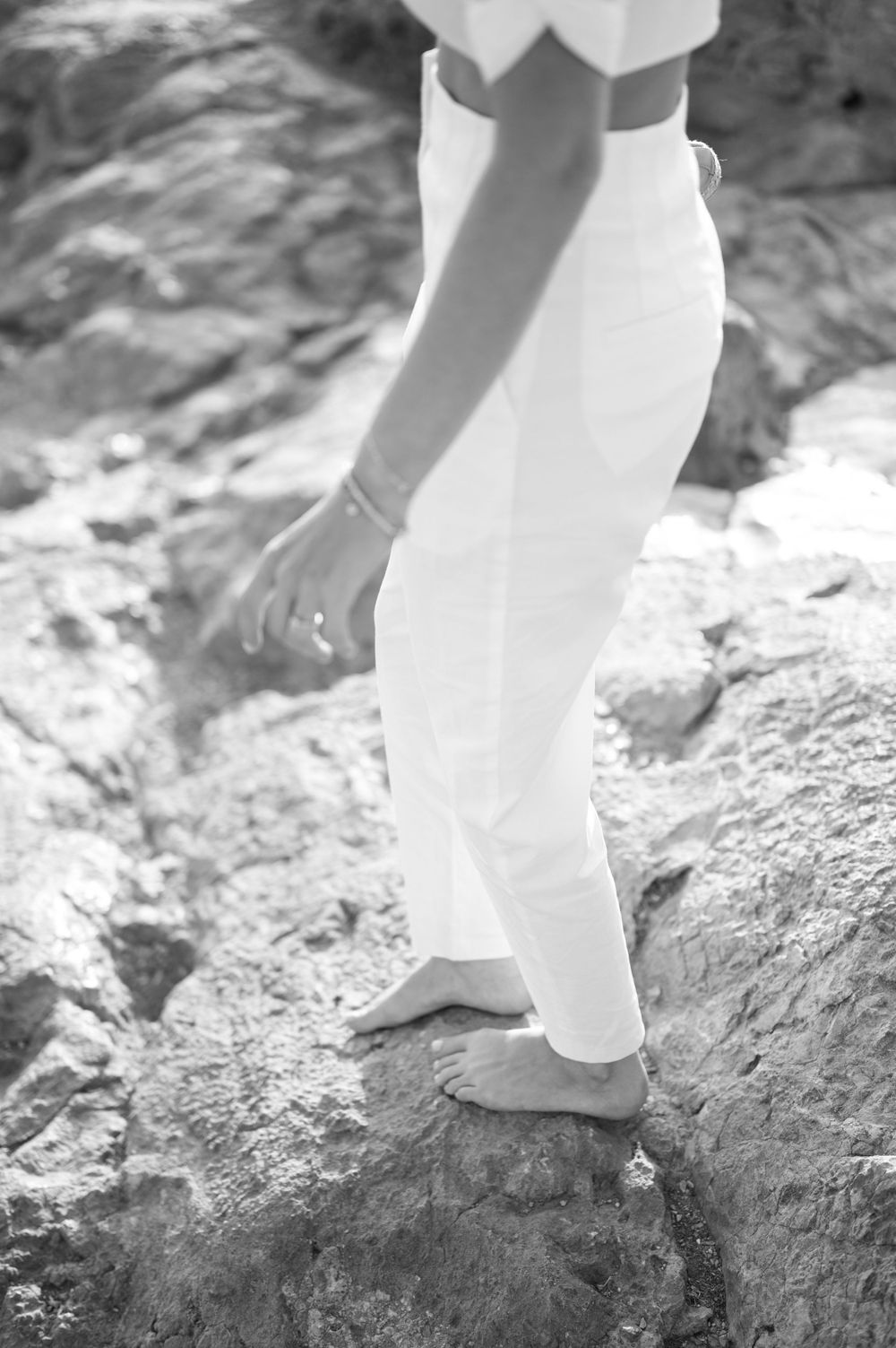 Black and white photo of person in white clothing walking barefoot on rocky terrain.