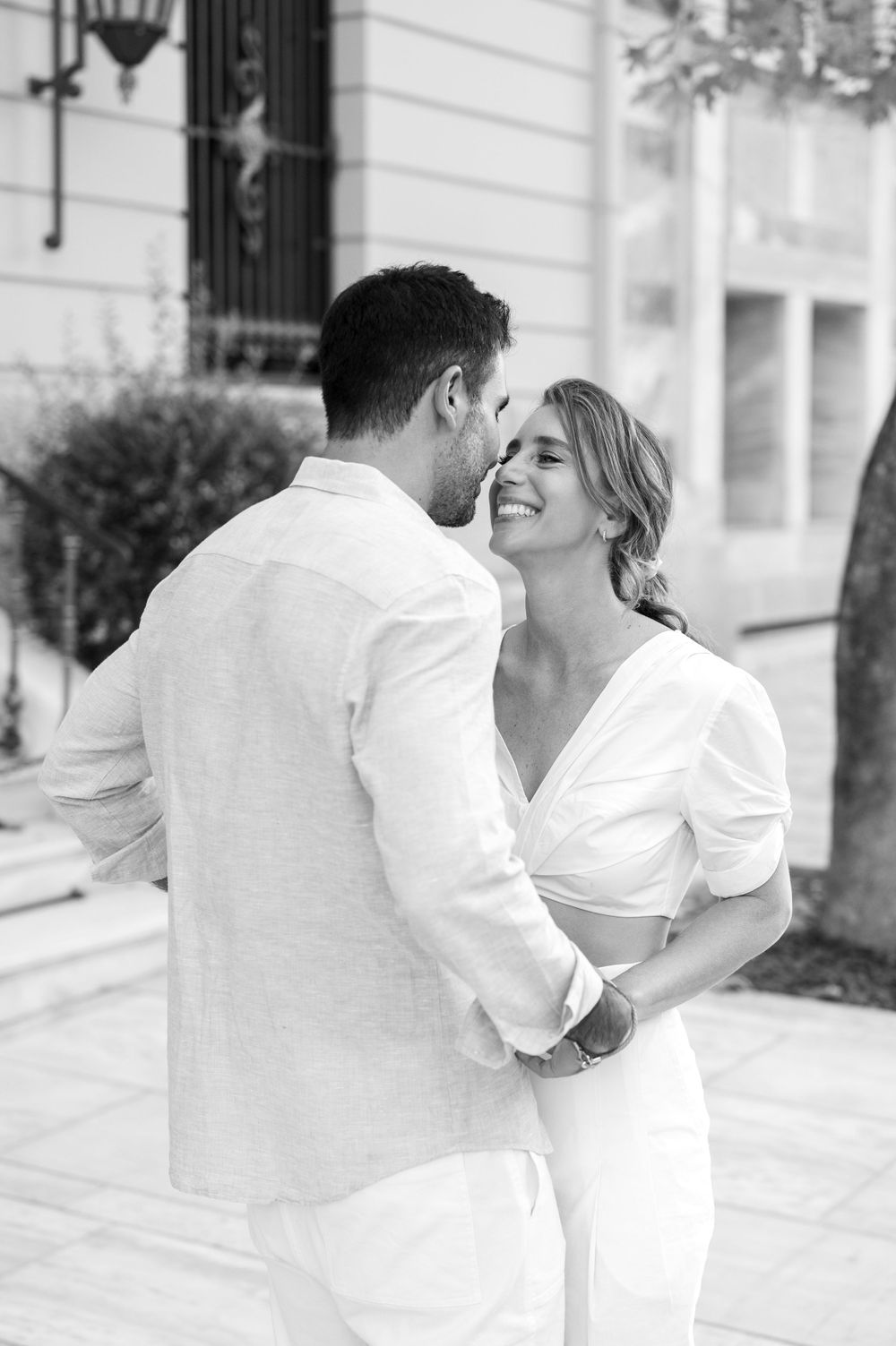 Black and white candid photo of couple sharing joyful moment in urban setting.