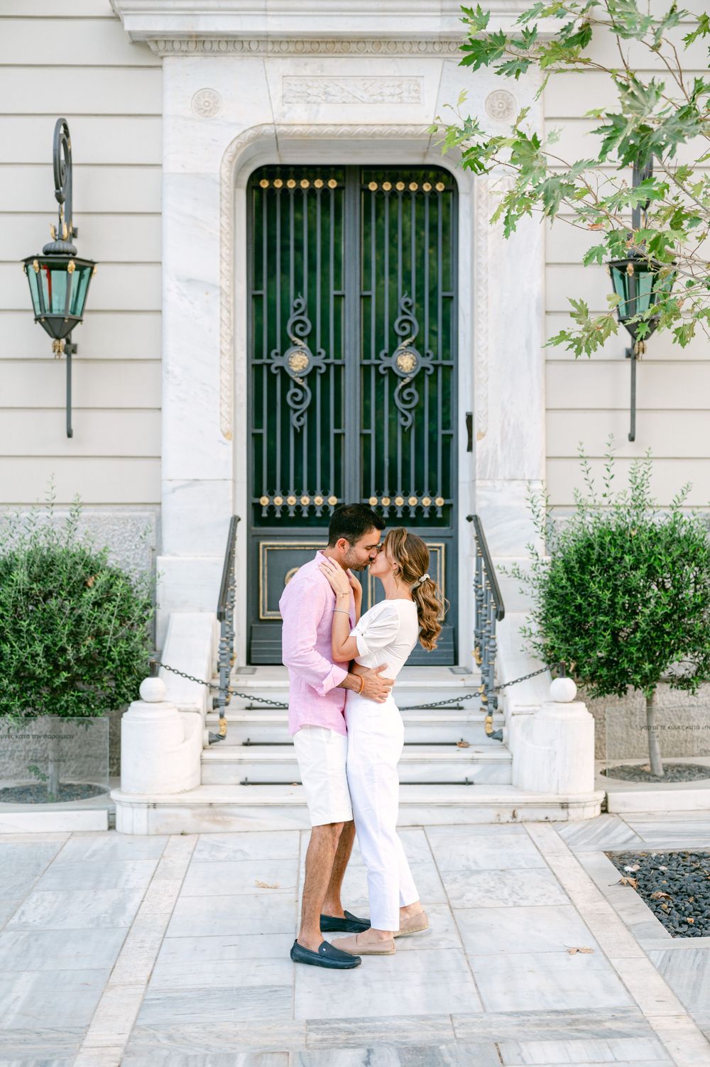 Couple sharing romantic moment in front of ornate green door with vintage lanterns.
