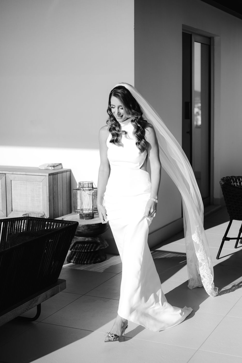 Black and white photo of a bride in flowing veil walking through a modern interior.