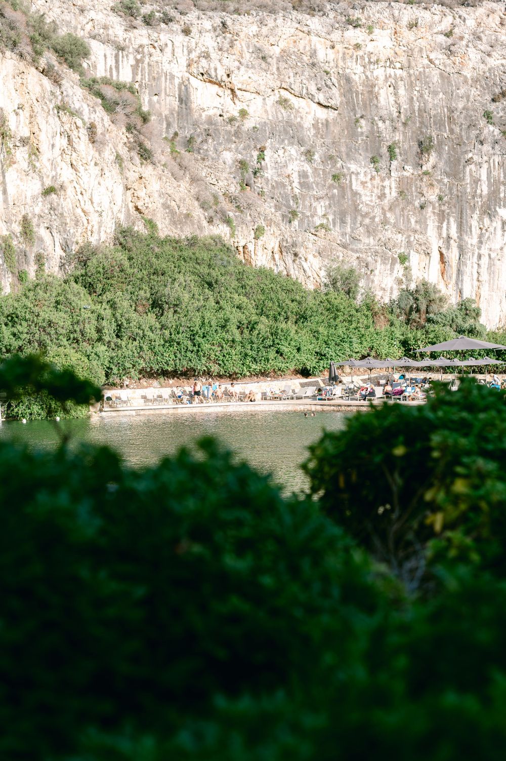 A scenic view of a limestone cliff face with a beach and swimming area nestled at its base.