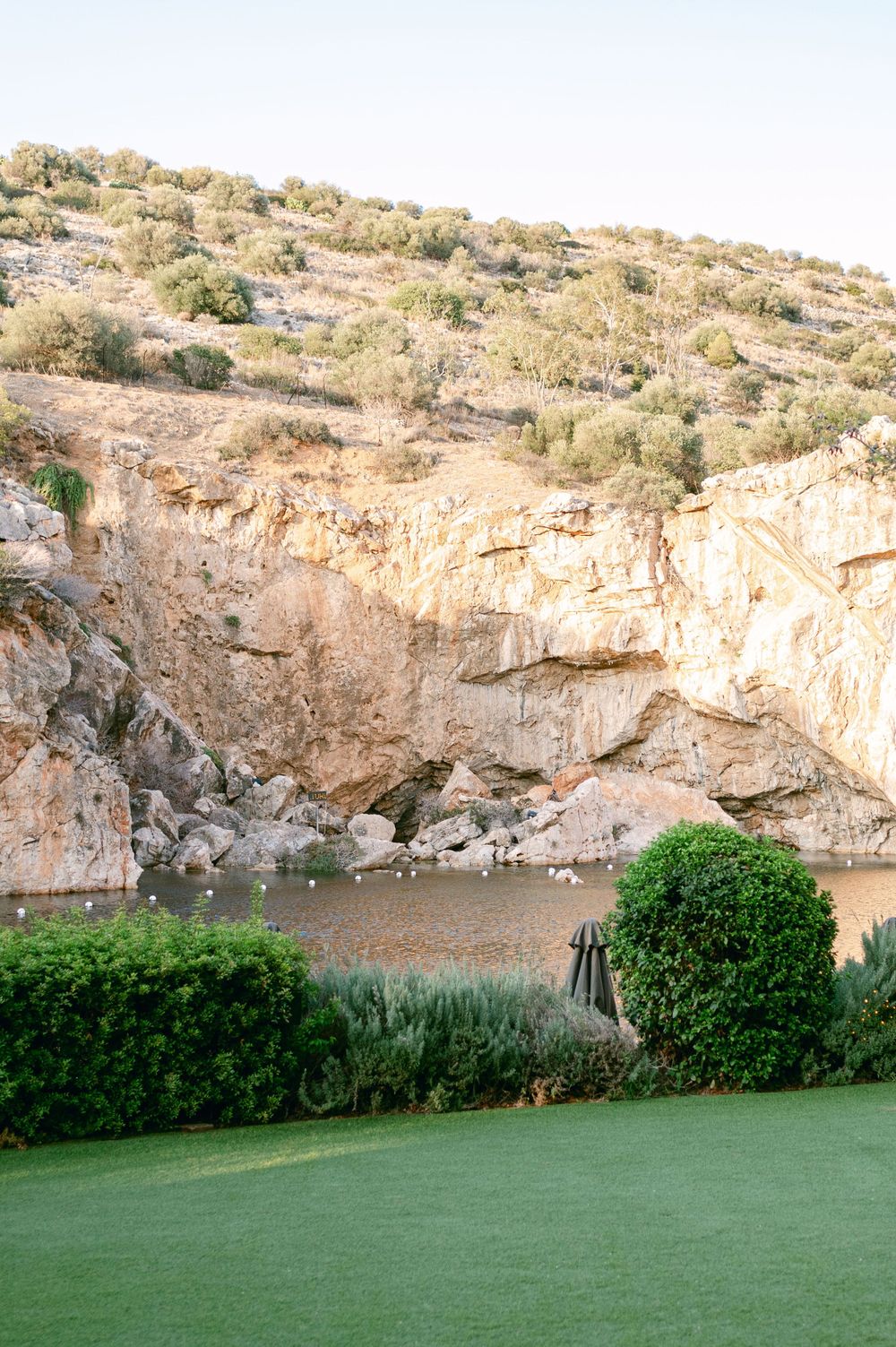 A dramatic rocky cliff formation overlooking a serene water area with manicured green lawn in foreground.