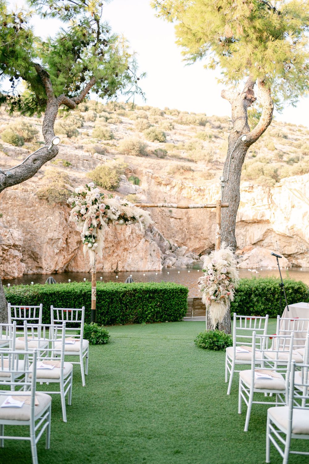 An elegant outdoor wedding ceremony setup with white chairs and floral arrangements against a rocky backdrop.