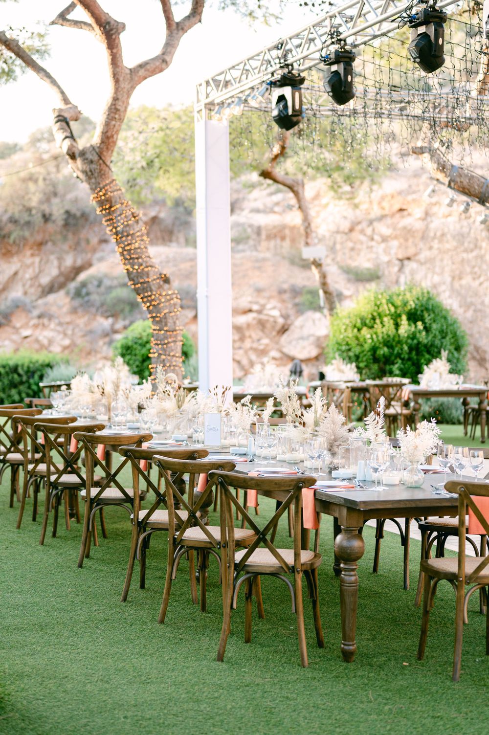 Rustic wooden dining tables set up outdoors with hanging lights and natural decor elements.