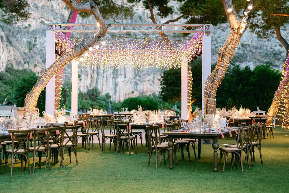An outdoor wedding reception venue decorated with romantic string lights and elegant table settings on a grassy lawn.