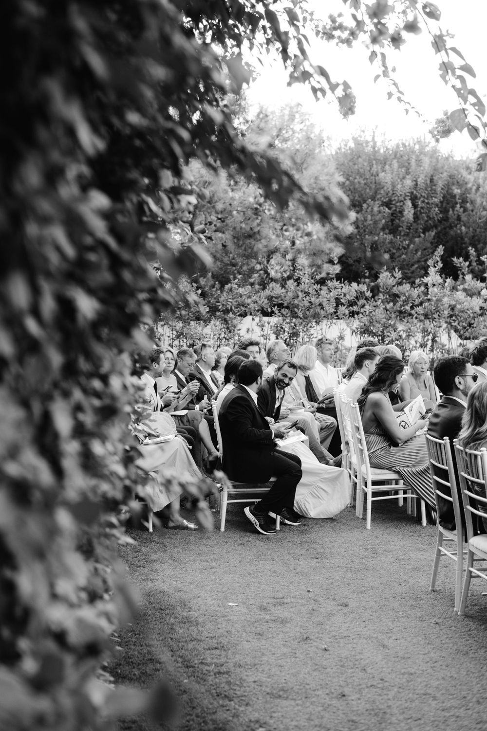 Black and white photo of wedding guests seated in white chairs during an outdoor garden ceremony.