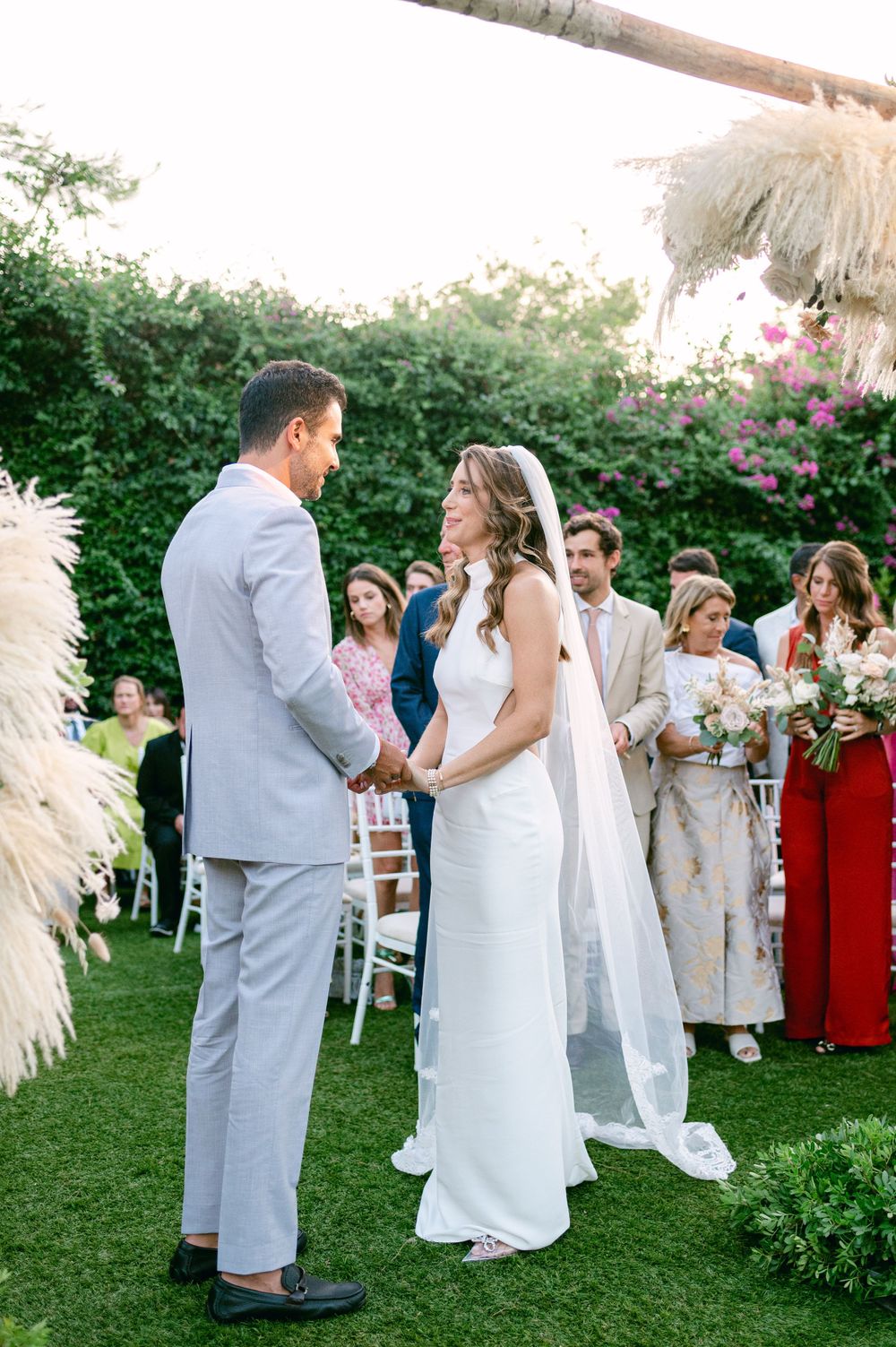 An outdoor wedding ceremony with white chairs and floral decorations against a backdrop of green hedges.