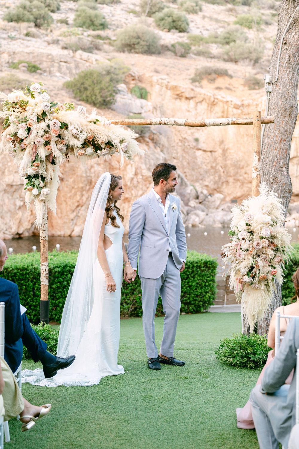 A wedding ceremony setup featuring white floral arrangements against dramatic desert cliffs.
