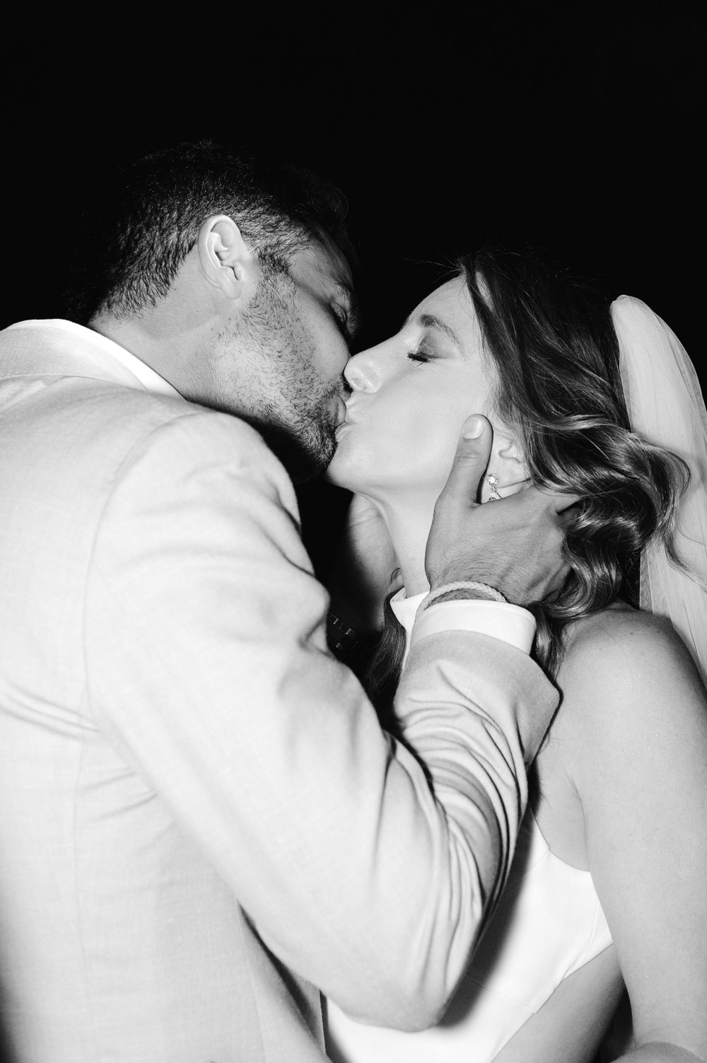 A romantic black and white portrait of newlyweds sharing their first kiss.