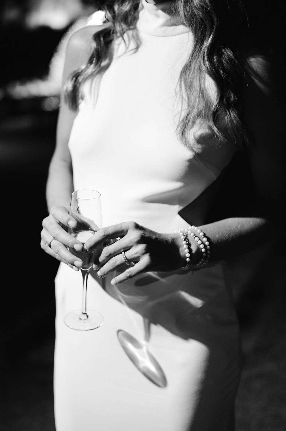 A close-up black and white photo shows a woman in white holding a champagne glass.