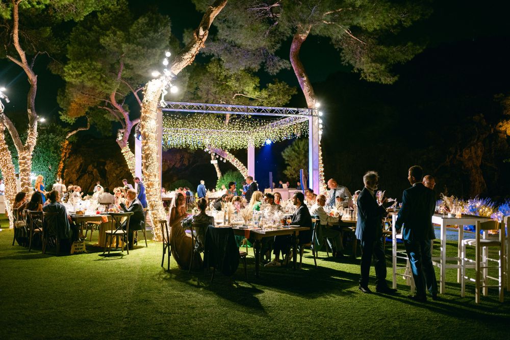 Wedding reception dinner under string lights with guests seated at long tables outdoors.