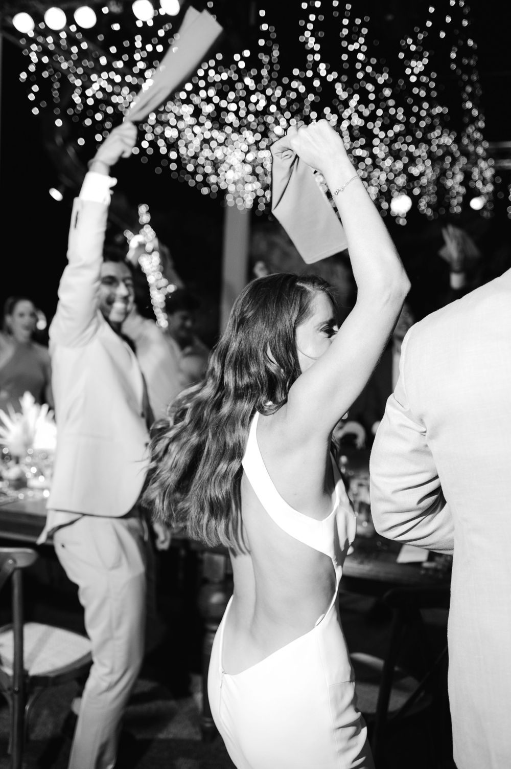 Partygoers dance with raised arms under a sparkling light display at a celebration.