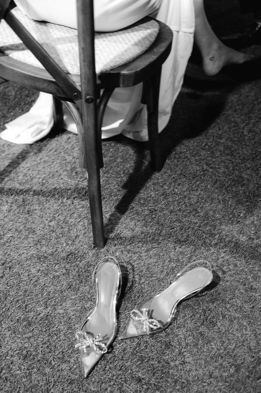 A pair of embellished silver shoes left on the ground next to a wooden chair leg.