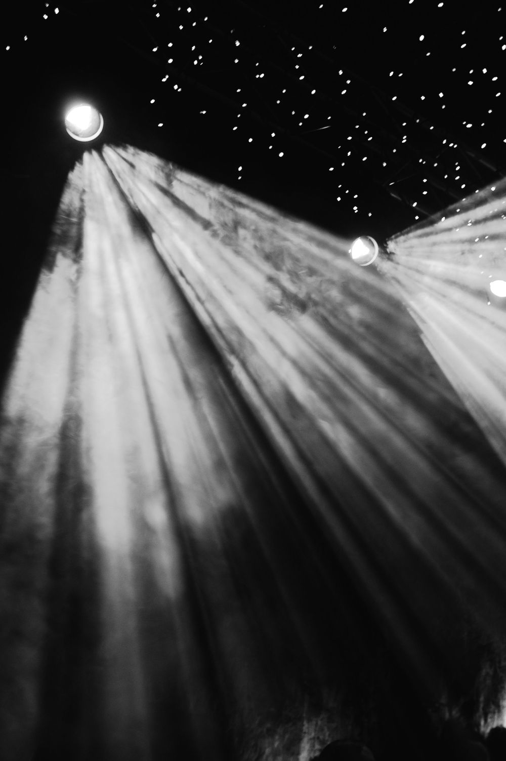 Dramatic black and white photograph of spotlights creating beams through a starry atmosphere.