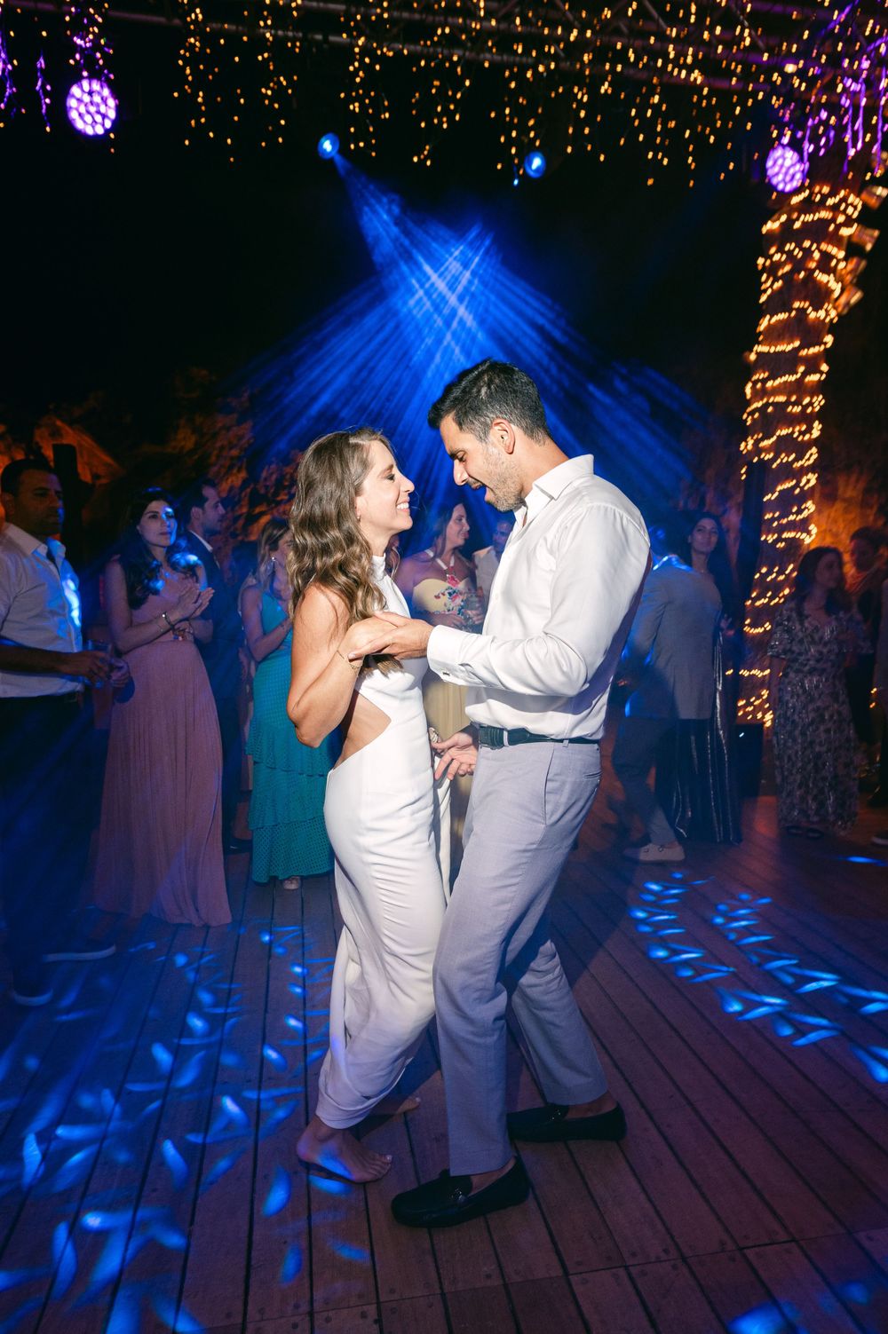 Couple shares an intimate dance under blue lighting and twinkling golden lights.