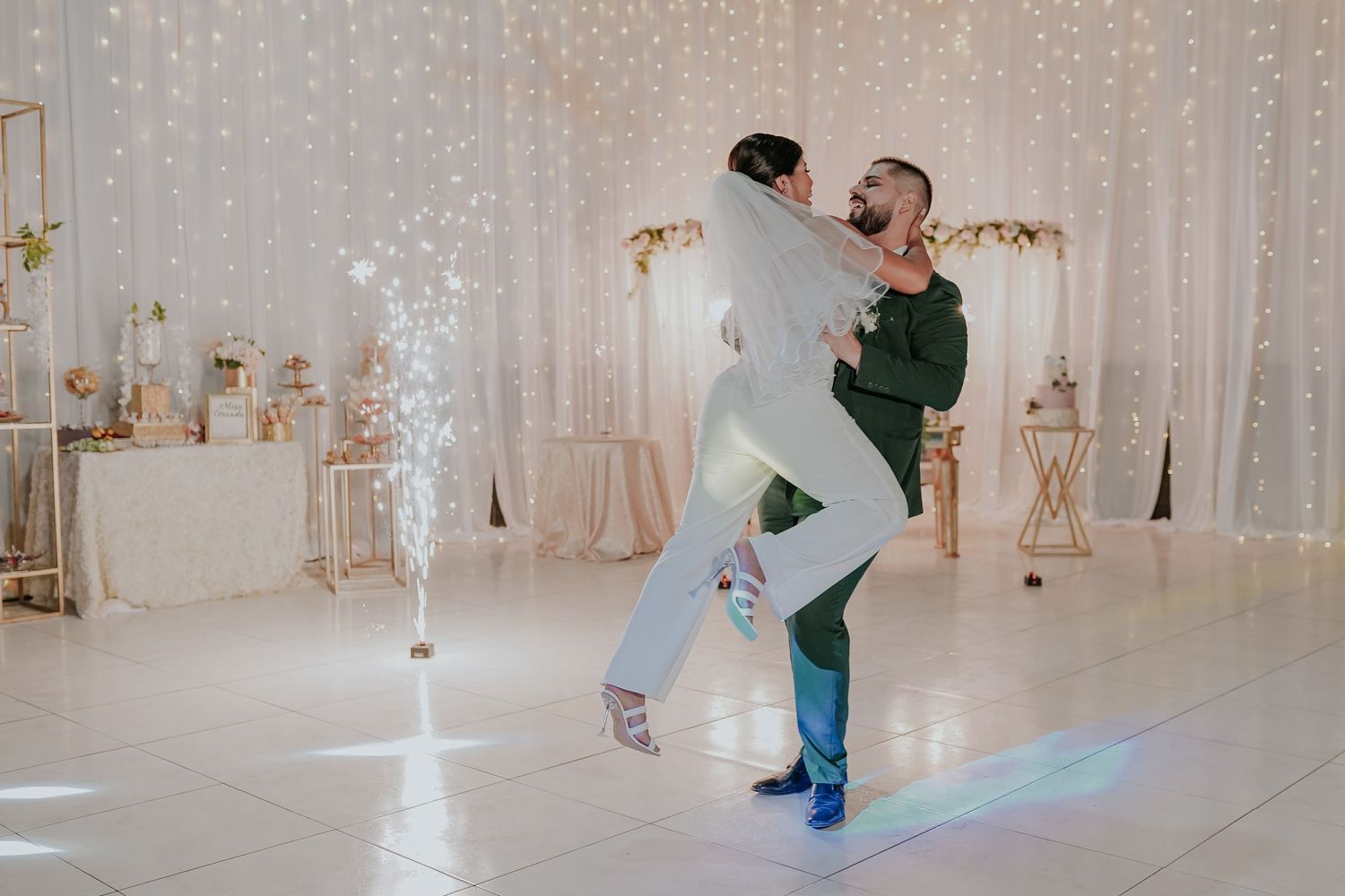 Joyful dancing moment captured during wedding reception with white decor and fairy lights.