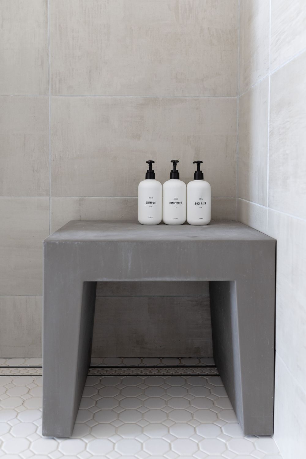 Three white pump bottles arranged on a modern gray concrete bench in a minimalist bathroom.