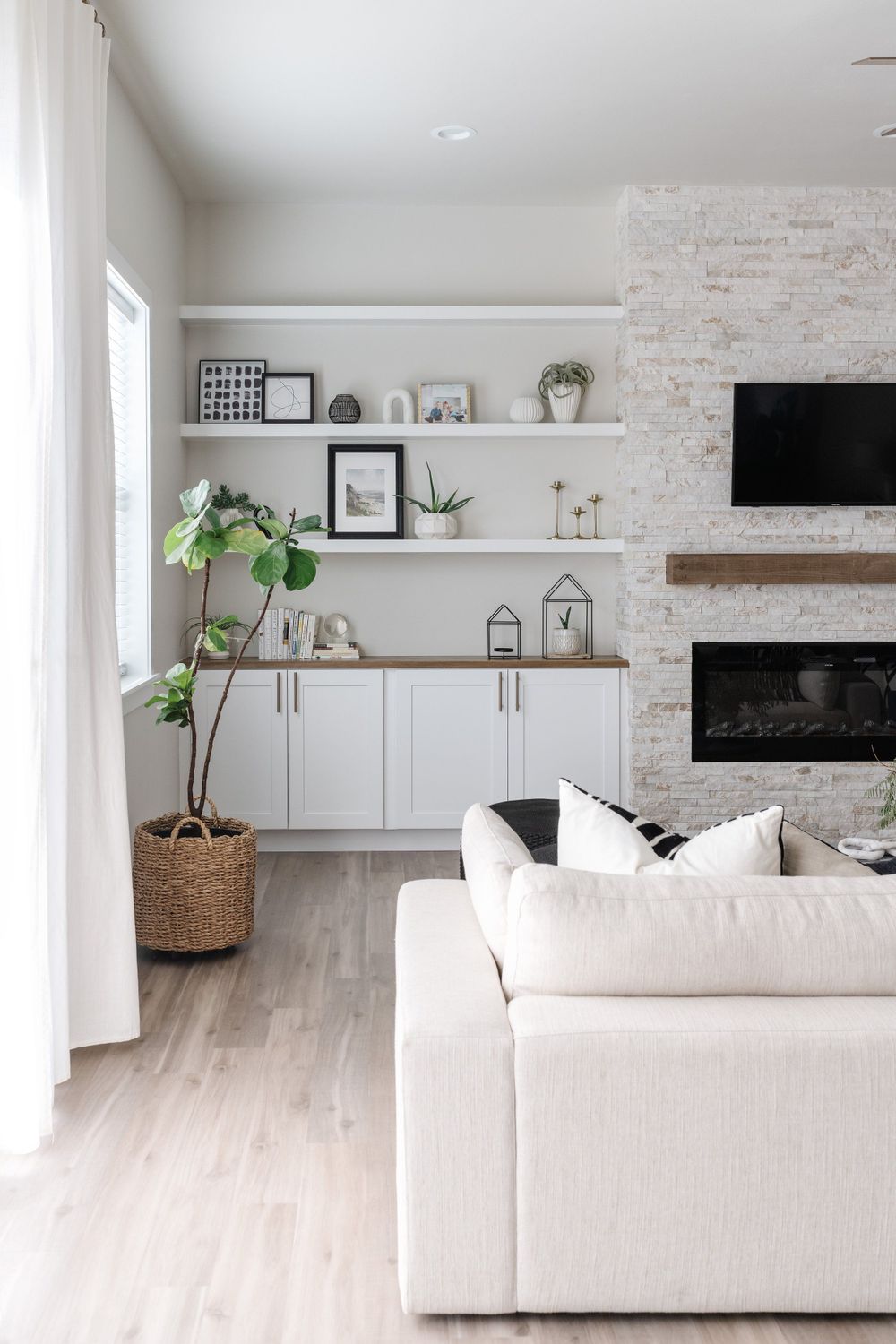 Contemporary living room with white built-ins, stone fireplace, and light hardwood floors.