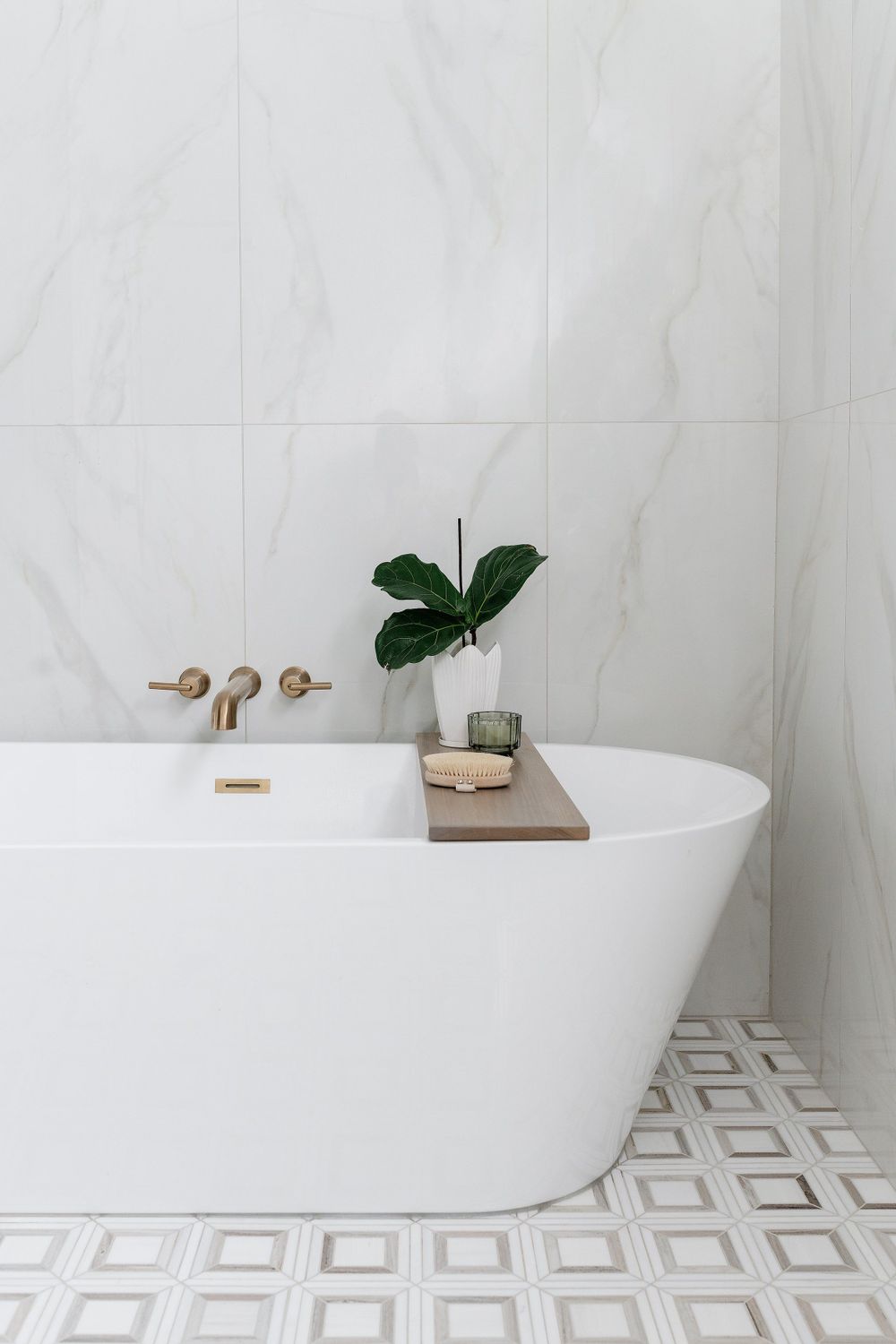 Freestanding white bathtub with brass fixtures and geometric tile floor in modern bathroom.