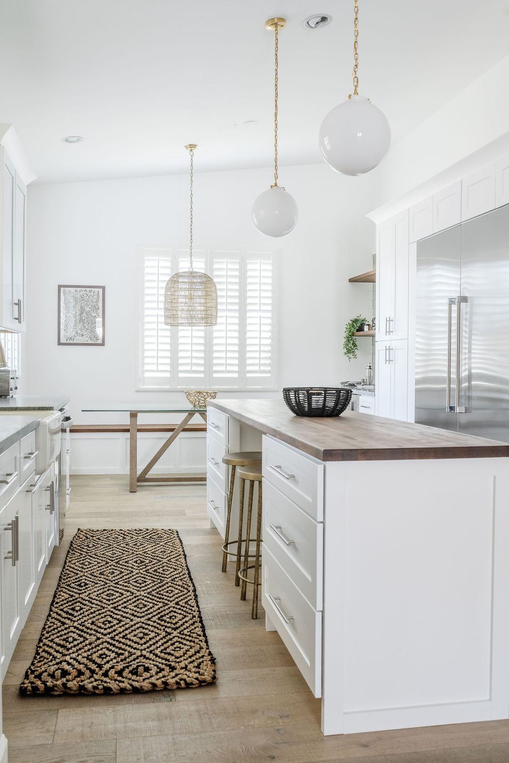 Modern white kitchen with wood countertops, geometric runner and globe pendant lights.