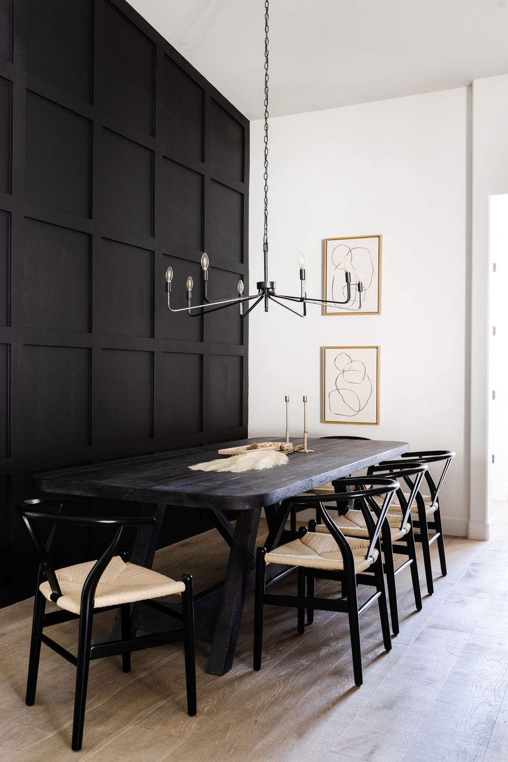 Modern dining room featuring black accent wall and contemporary chandelier over dark table.