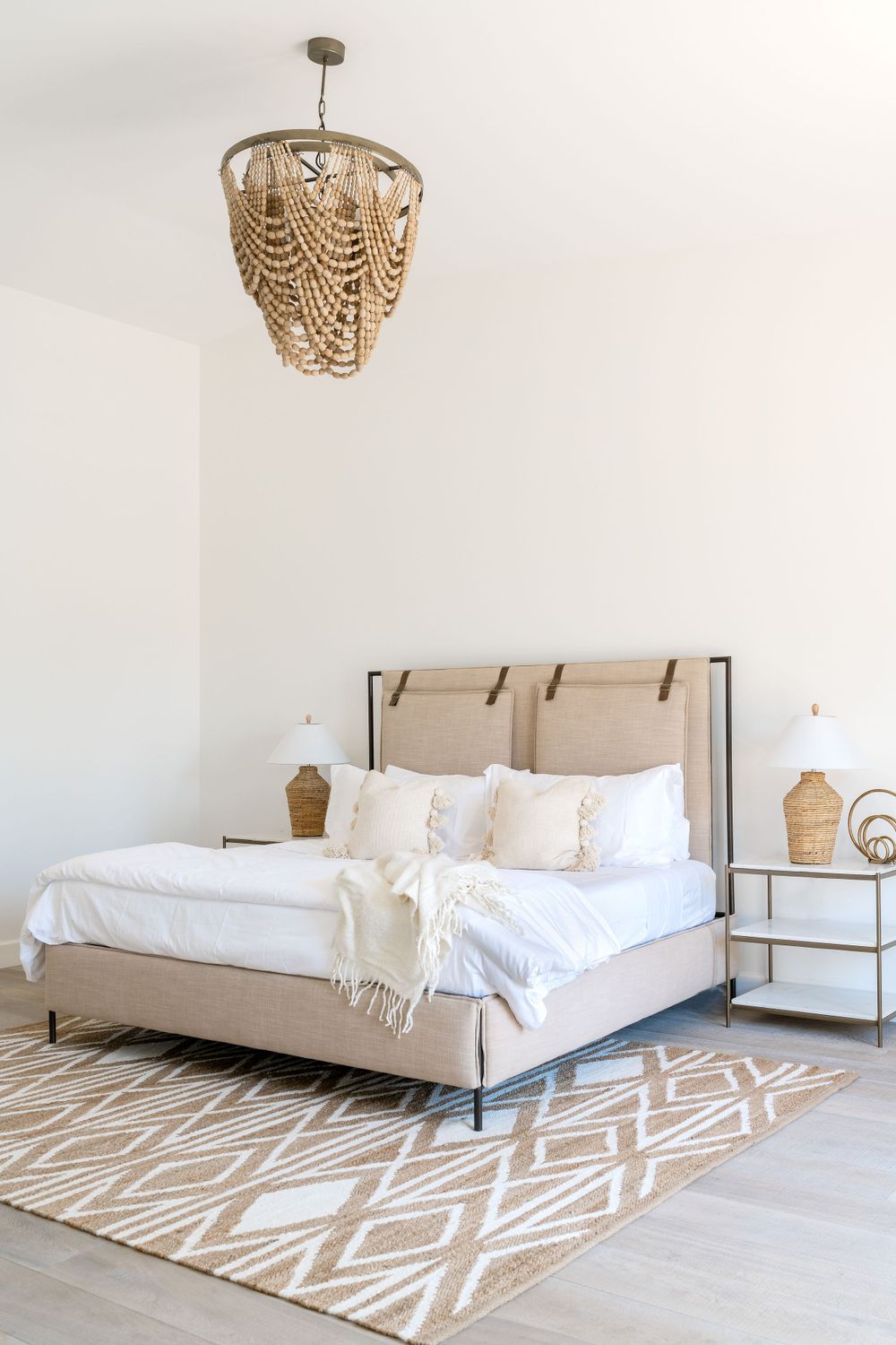 Neutral bedroom with beige upholstered bed, geometric rug and woven chandelier.