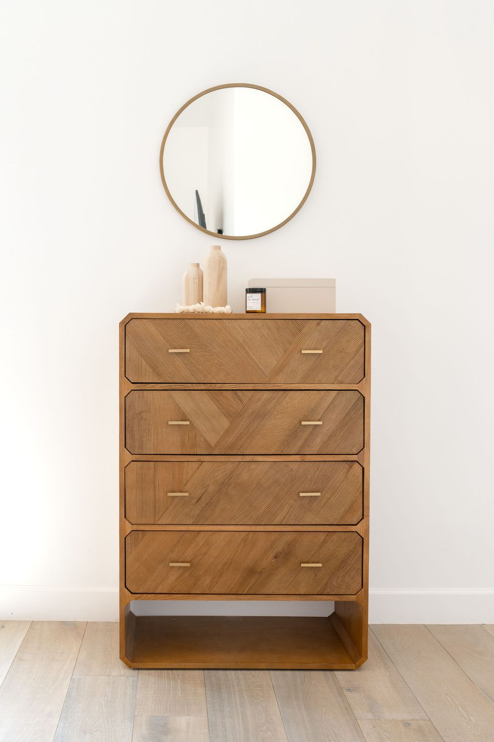 Modern wooden dresser with chevron pattern and round gold mirror above.