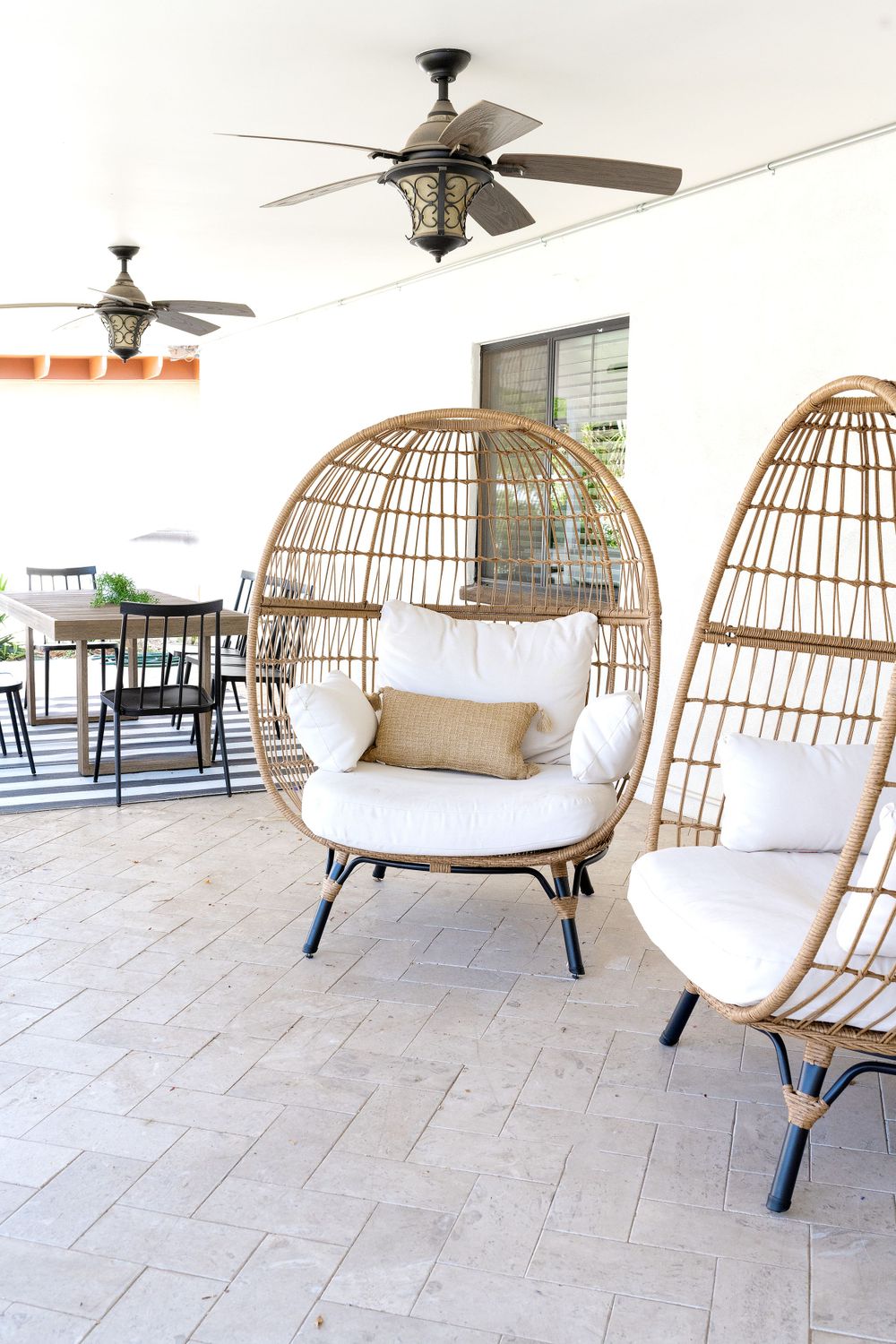 Outdoor patio area with three rattan egg chairs featuring white cushions and ceiling fans overhead.
