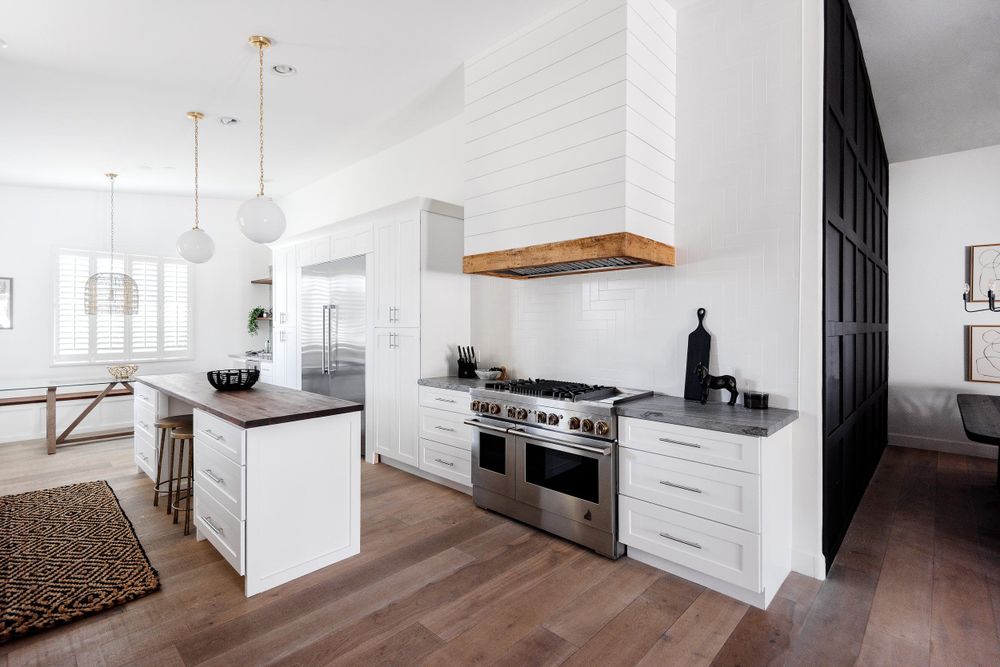 Contemporary white kitchen with wood accents, black pantry wall and pendant lighting.