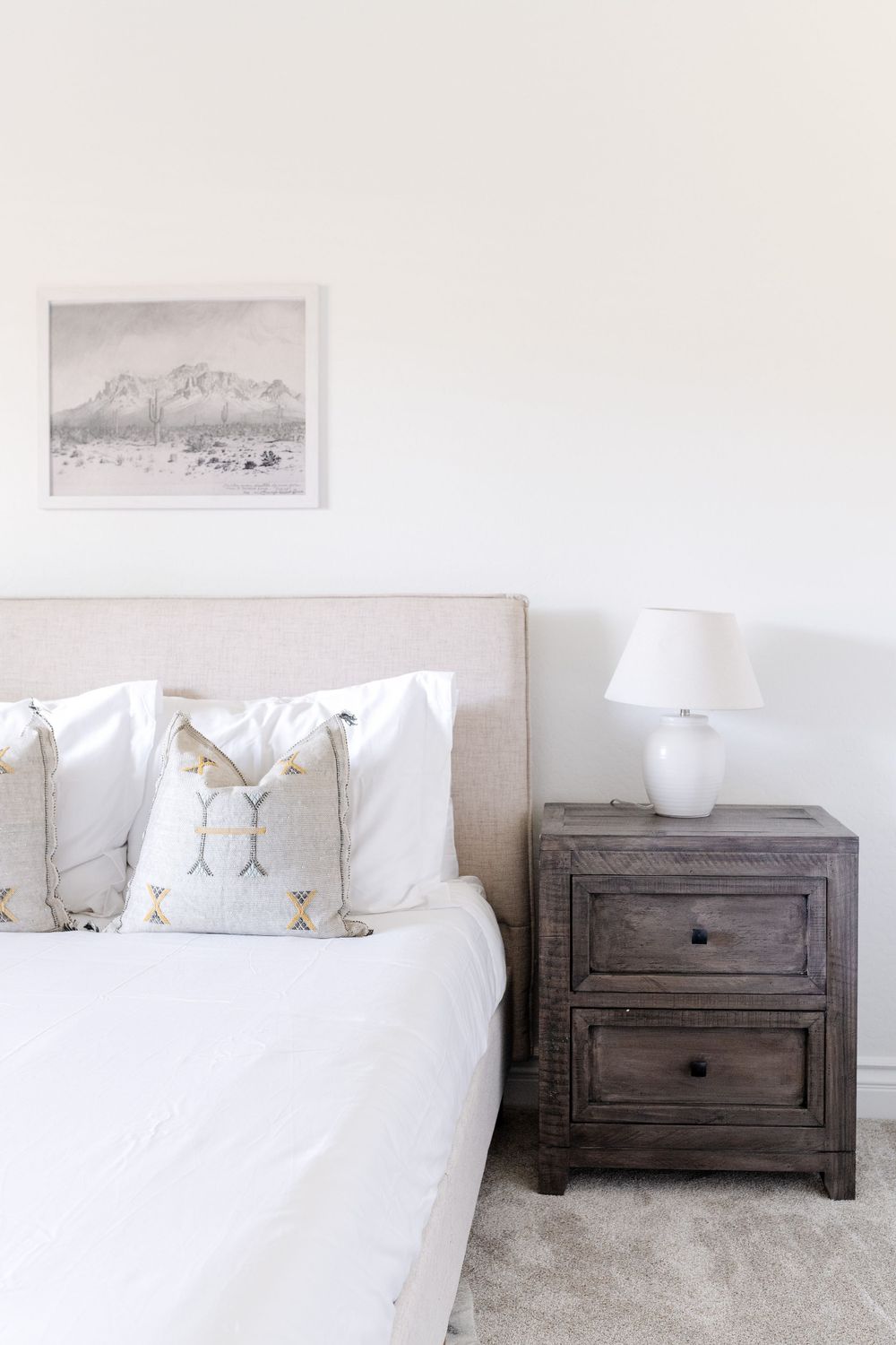 Minimalist bedroom with upholstered headboard, bird pillows and mountain artwork above.