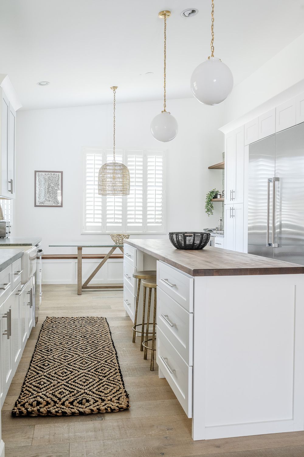 Bright white kitchen with modern pendant lights, wooden countertops, and a geometric patterned runner.
