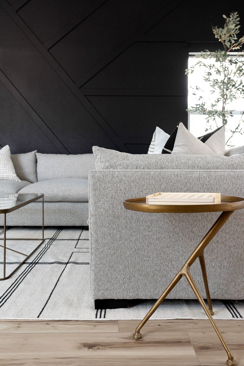 Modern living room with grey sectional, black accent wall and gold side table.